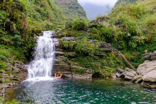 Fototapeta Naklejka Na Ścianę i Meble -  A couple holds each other while swimming under the Du Gia waterfall in Ha Giang in northern Vietnam