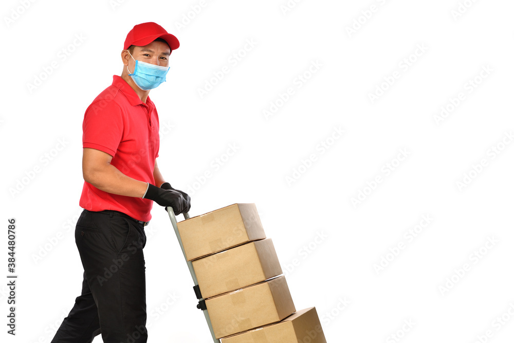 Happy young Asian delivery man in red uniform, medical face mask, protective gloves pushing a hand truck with boxes isolated on white background. Delivery guy give parcel shipment. Safe delivery Happy young Asian delivery man in red uniform, medical face mask, protective gloves pushing a hand truck with boxes isolated on white background. Delivery guy give parcel shipment. Safe delivery