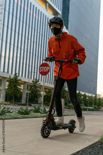 Boy wearing face mask and helmet rides electric scooter