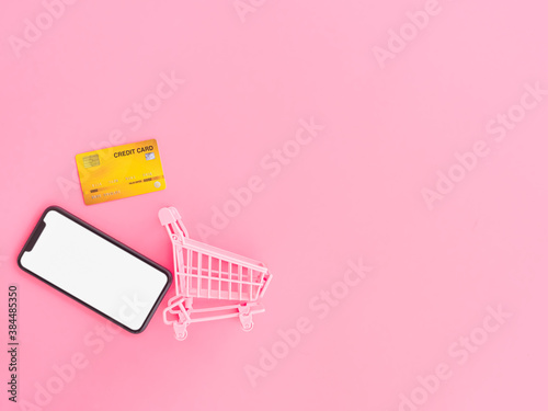 shopping and payment online concept from credit cards, shopping cart and blank smartphone on pink pastel color background.