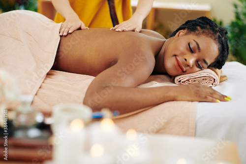 Smiling young Black woman enjoying relaxing back massage in beauty salon