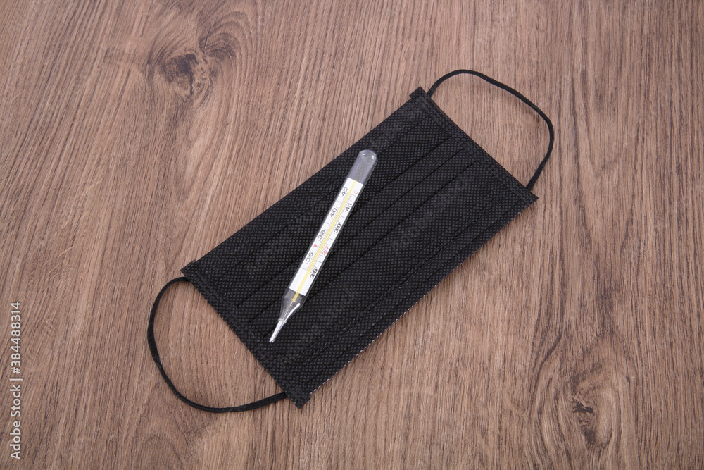 A black medical mask and a clinical thermometer A black medical mask and a clinical thermometer