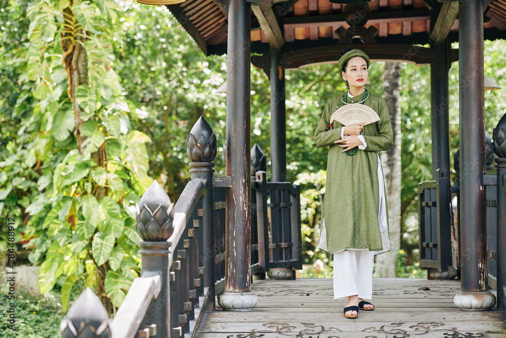 Beautiful young Vietnamese woman in traditional dress visiting historical place