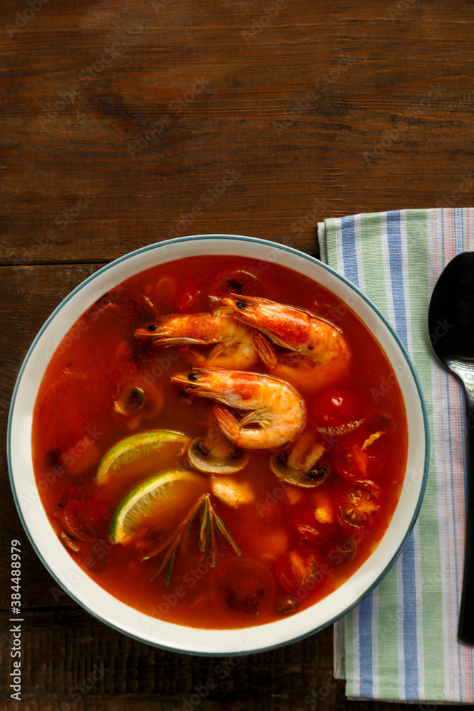 Tom yam soup with shrimp and lime in a light plate next to a spoon on a napkin. Tom yam soup with shrimp and lime in a light plate next to a spoon on a napkin.