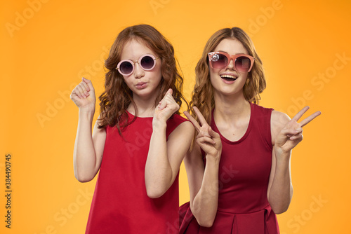 Happy woman and little girl in red dress are having fun on a yellow background fashion emotions sisters fun Copy Space.