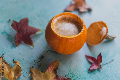 pumpkin spice latte in pumpkin cup with fall leaves on turquoise background