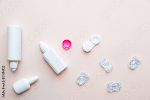 Contact lenses, lens solution and lens containers on a light pink background. Health care concept top view copy space