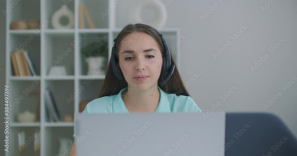 Happy young business woman wears headset talks to web camera making distance online video conference call. Female internet teacher doing distant chat working from home. Telework concept. Webcam view Happy young business woman wears headset talks to web camera making distance online video conference call. Female internet teacher doing distant chat working from home. Telework concept. Webcam view