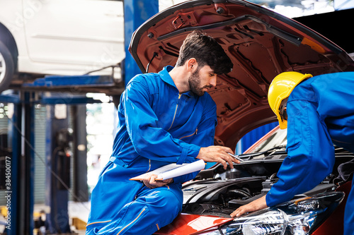 Mechanic checking the opened hood car with his assistant. Auto car repair service center. Professional service.