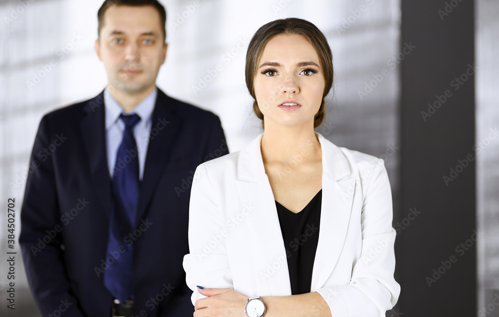 Young beautiful businesswoman is standing in an office with a male colleague at the background. Concept of success in a business