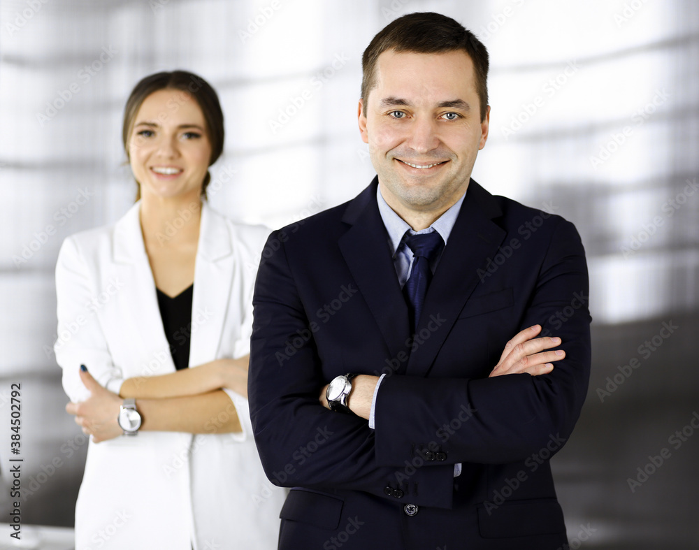 Portrait of a friendly middle aged businessman in a dark blue suit, standing with crossed arms together with a colleague in a modern office. Concept of success in a business Portrait of a friendly middle aged businessman in a dark blue suit, standing with crossed arms together with a colleague in a modern office. Concept of success in a business