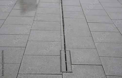 large-format paving made of gray granite. the water is drained in the rain through a slotted stainless steel channel which is sunk under the surface of the tile. photo