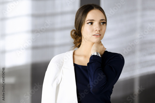 Friendly young business woman or female student dressed in white suit is standing straight and posing at camera. Lifestyle and diverse people concept