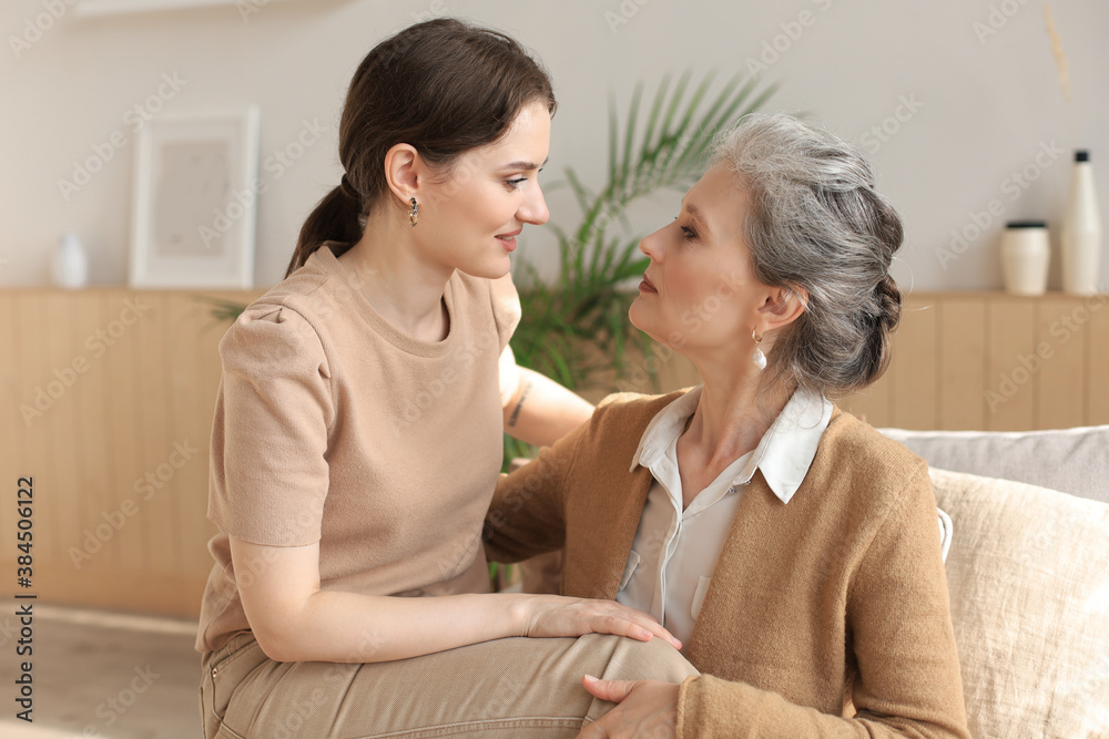 Elderly middle mother sitting on couch with joy holding adult daughter on knees. Happy trusted relations. Family concept. Elderly middle mother sitting on couch with joy holding adult daughter on knees. Happy trusted relations. Family concept.