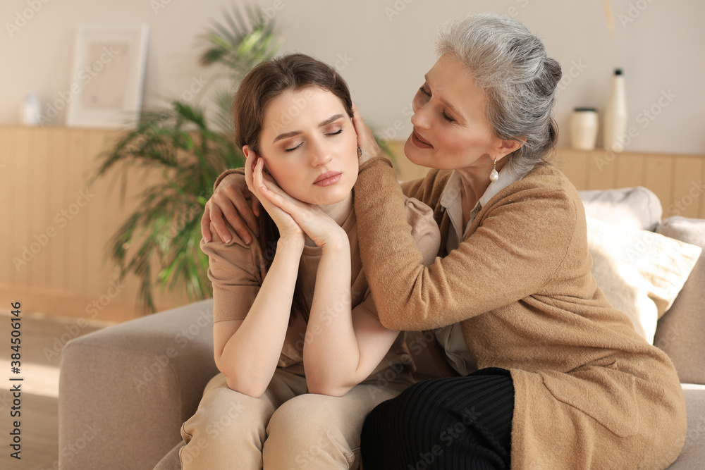 Middle aged mother is embracing her daughter, comforting upset frustrated daughter with closed eyes, touching cheeks, sitting on couch at home. Happy trusted relations. Family concept. Middle aged mother is embracing her daughter, comforting upset frustrated daughter with closed eyes, touching cheeks, sitting on couch at home. Happy trusted relations. Family concept.