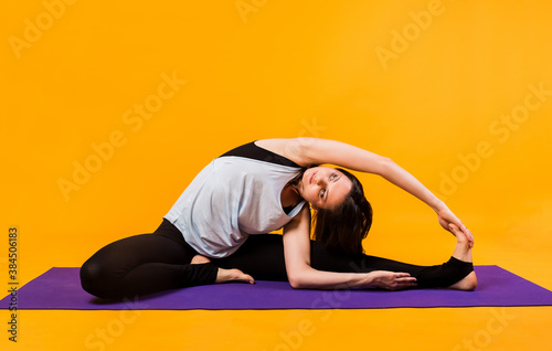 a woman in a tracksuit performs stretching on a purple Mat on an orange background