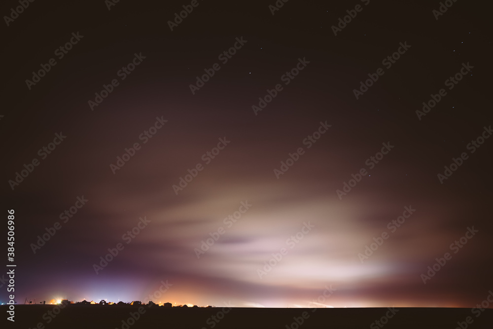 Night Sky With Rare Glowing Stars Shining Through The Cloudiness Overcast Above Countryside Town Landscape. Rural Field Meadow In Early Spring Night Sky With Rare Glowing Stars Shining Through The Cloudiness Overcast Above Countryside Town Landscape. Rural Field Meadow In Early Spring
