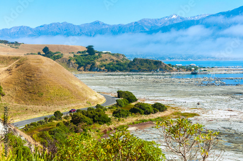 View from point Kean over beautiful scenic road along Pacific Ocean coast in Kaikoura with mountains in the morning mist clouds on vivid blue sky, Marlborough Region, South Island, New Zealand photo