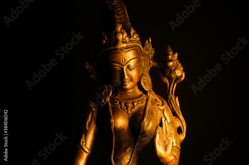 Close up of isolated illuminated hindu Shiva god golden bronze statue with raised hand on blank black background