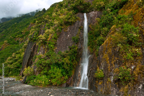 Waterfall among rocks and green plants near Franz Josef Glacier  South Island  New Zealand