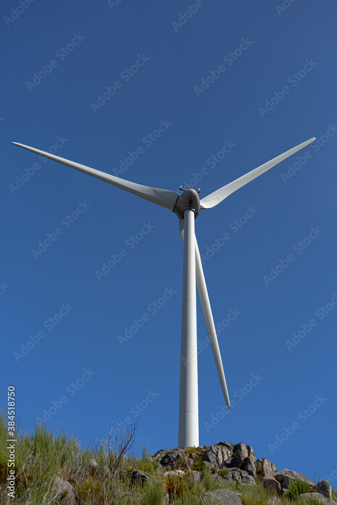 View of a wind turbine on top of mountains, blue sky as background View of a wind turbine on top of mountains, blue sky as background