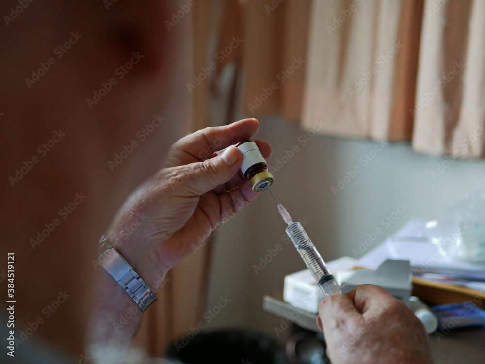 An old man's hands carefully pulling the medicine into the syringe by himself at home - self injecting in the elderly - obrazy, fototapety, plakaty 