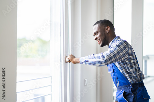 African Repairman In Overalls Installing Window