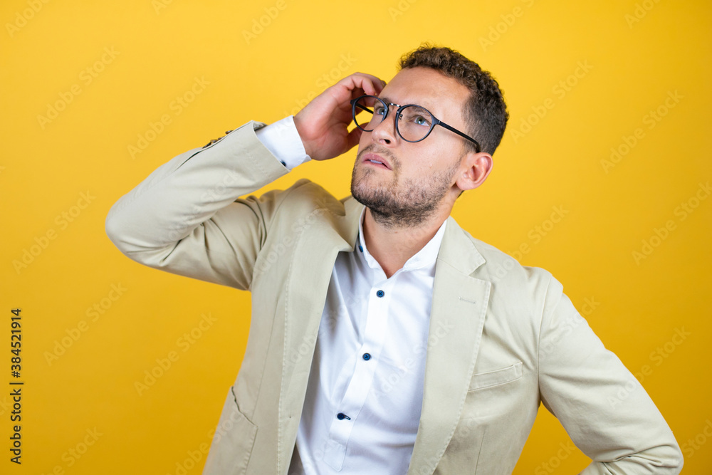 Young handsome businessman wearing suit over isolated yellow background putting one hand on her head smiling like he had forgotten something Young handsome businessman wearing suit over isolated yellow background putting one hand on her head smiling like he had forgotten something