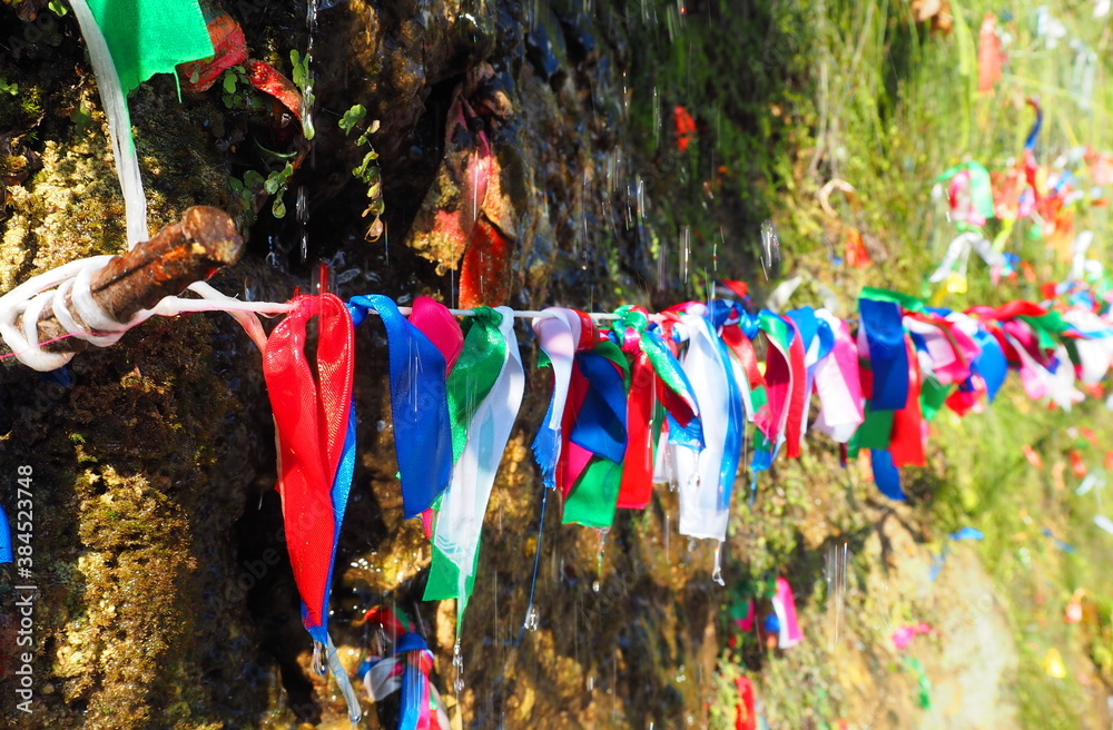 Colored ribbons hang on a rope. Beautiful ribbons hang near the mountain and the water flows down