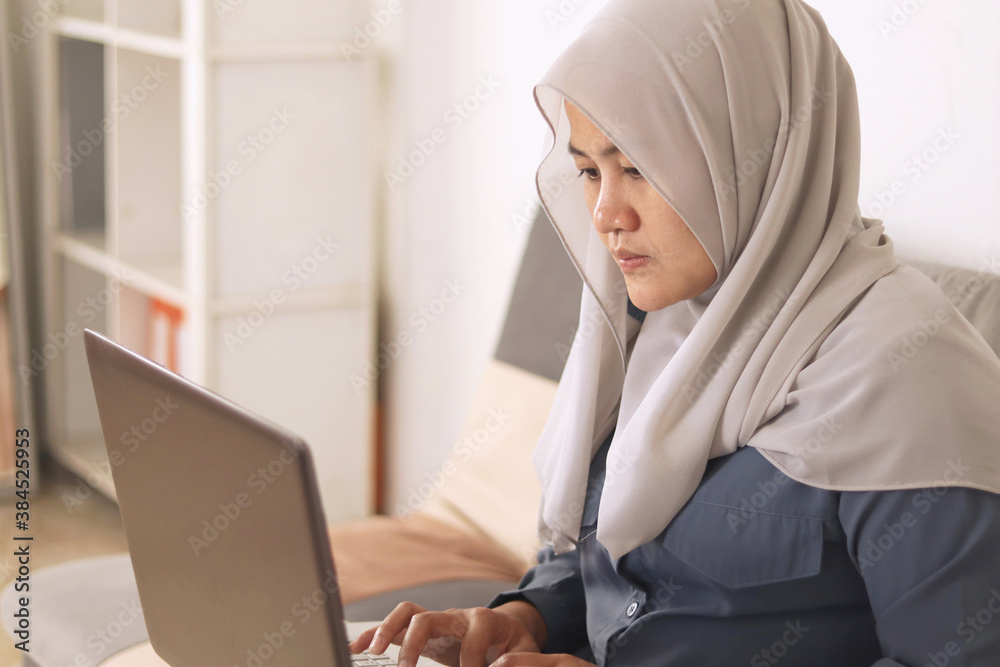 Asian muslim woman wearing hijab smiling while typing on her laptop, work from home concept. Young successful female entrepreneur working at home Asian muslim woman wearing hijab smiling while typing on her laptop, work from home concept. Young successful female entrepreneur working at home