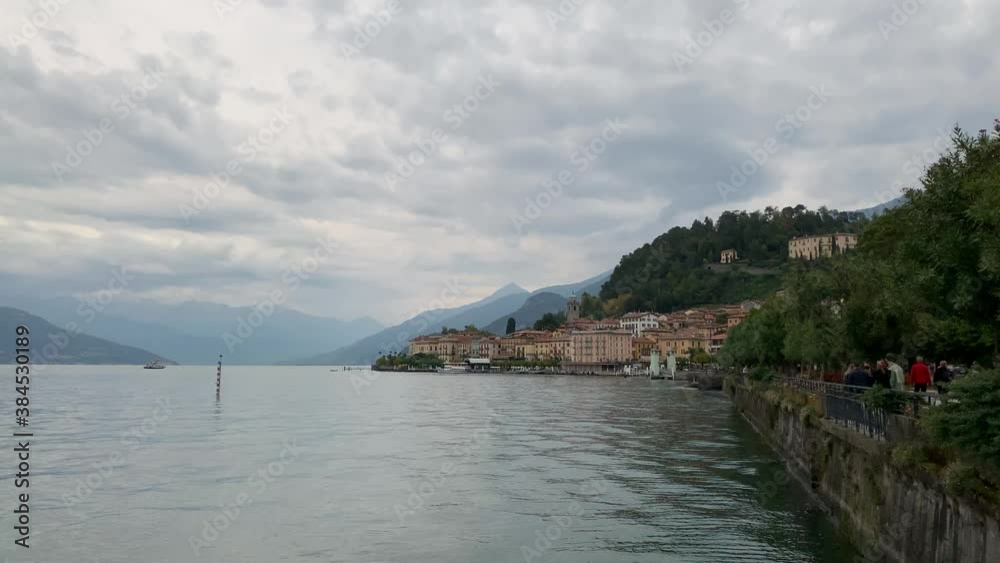 Dusk at Lake Como, from Bellagio, a beautiful alpine lake bathed in golden light with misty mountains scenery in the distance at ferry boats transporting passengers Dusk at Lake Como, from Bellagio, a beautiful alpine lake bathed in golden light with misty mountains scenery in the distance at ferry boats transporting passengers