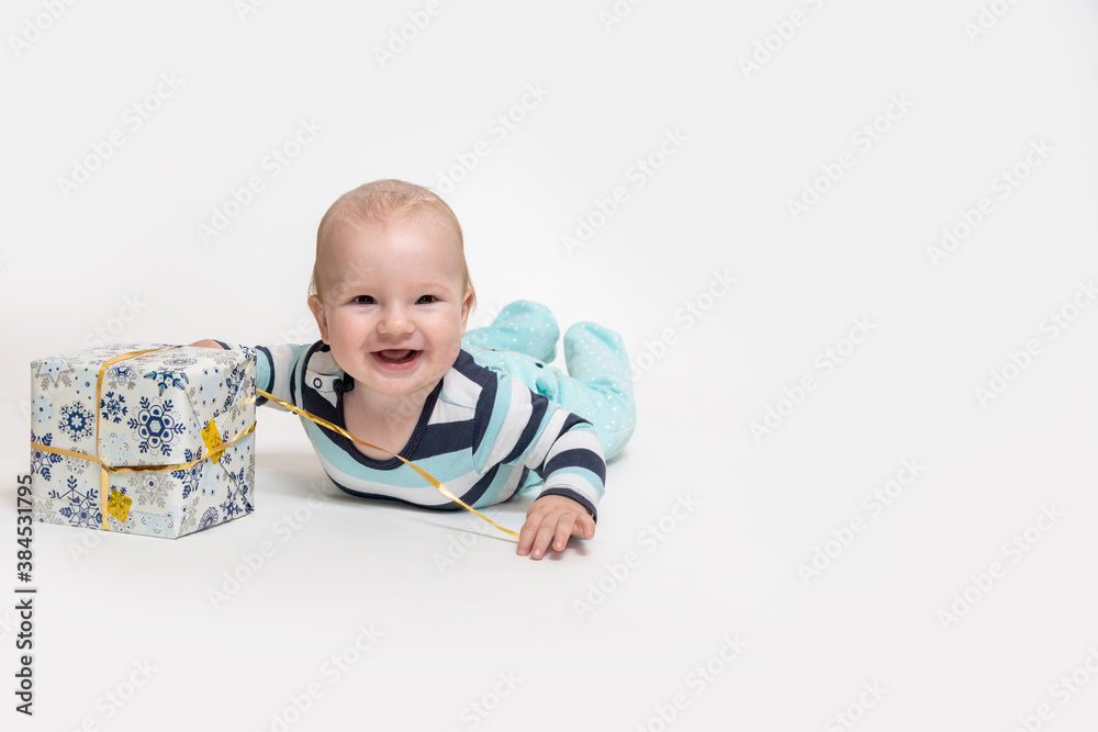Smiling toddler boy is an untying Christmas package lying on the floor. All is on the white background Smiling toddler boy is an untying Christmas package lying on the floor. All is on the white background