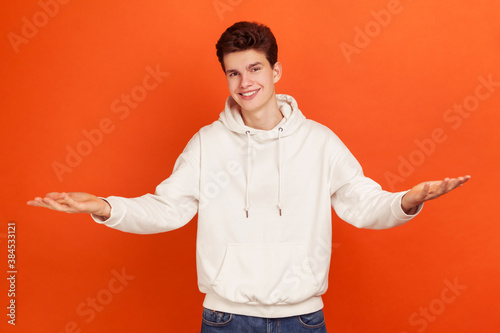 Fotografía Happy satisfied young man with generous smile in casual style hoodie widely spreading his arms welcoming dear guests, greeting