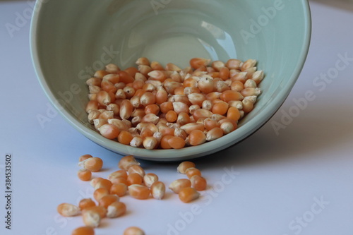 Corn seed in green ceramic bowl isolated on white background. Spilled seed pile.