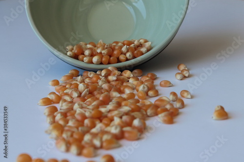 Corn seed in green ceramic bowl isolated on white background. Spilled seed pile.