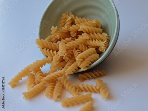 Uncooked raw Italian fusilli pasta in a ceramic bowl on white background. Side view.