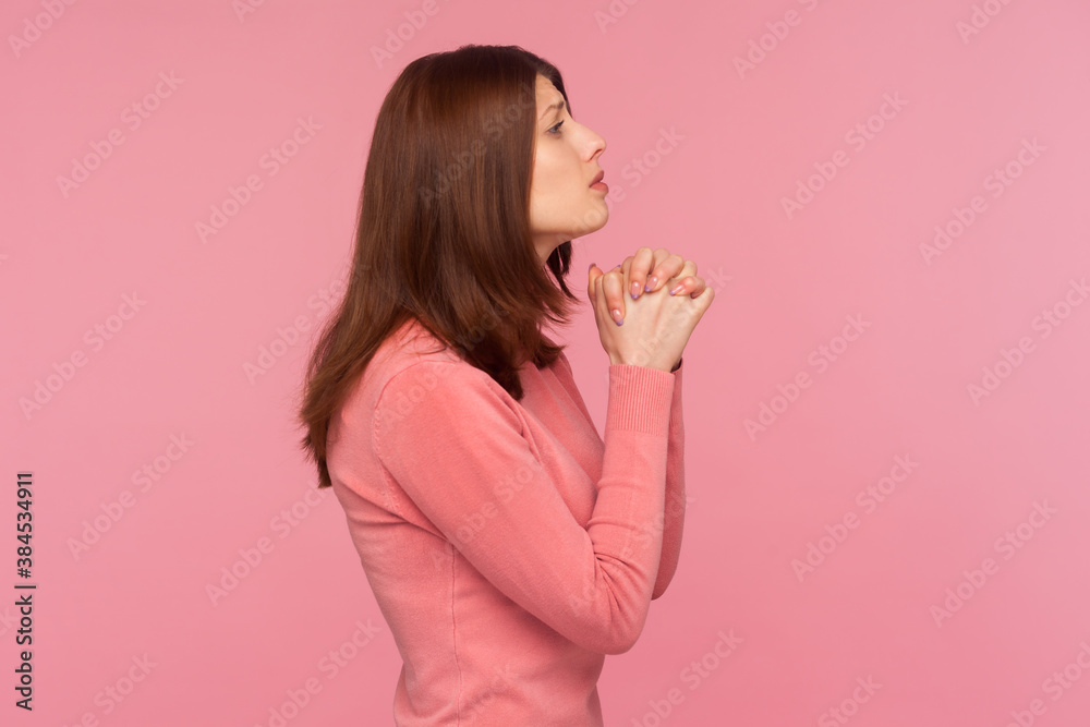 Profile portrait brunette woman in pink sweater praying god pressing hands, faith and religion. Indoor studio shot isolated on pink background Profile portrait brunette woman in pink sweater praying god pressing hands, faith and religion. Indoor studio shot isolated on pink background