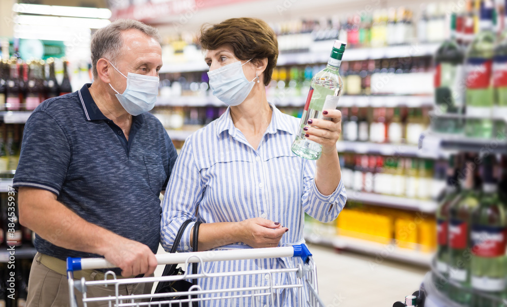 Pensioners in protective masks choose alcoholic beverages in supermarket