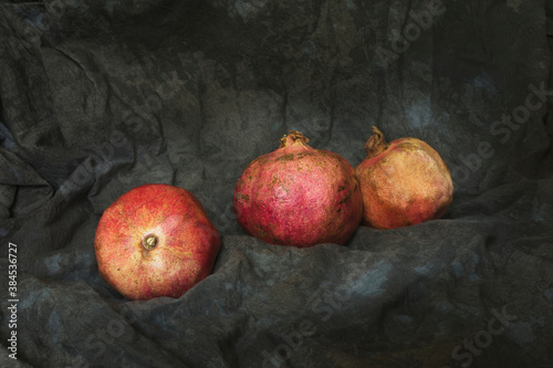 Still life with three pomegranates from organic farming, on a dark fabric background.