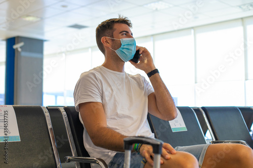 Young handsome man wearing mask in the airport with his mobile