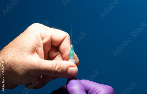 doctor removes protector medical needle, injection, syringe and purple glove, blue background