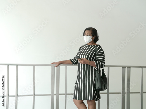 Woman with handbag and wearing face mask, standing and holding cellphone photo