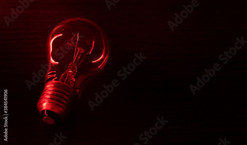 Incandescent light bulb in red light, bulb contour. Incandescent light bulb with tungsten filament on a black background in red light.