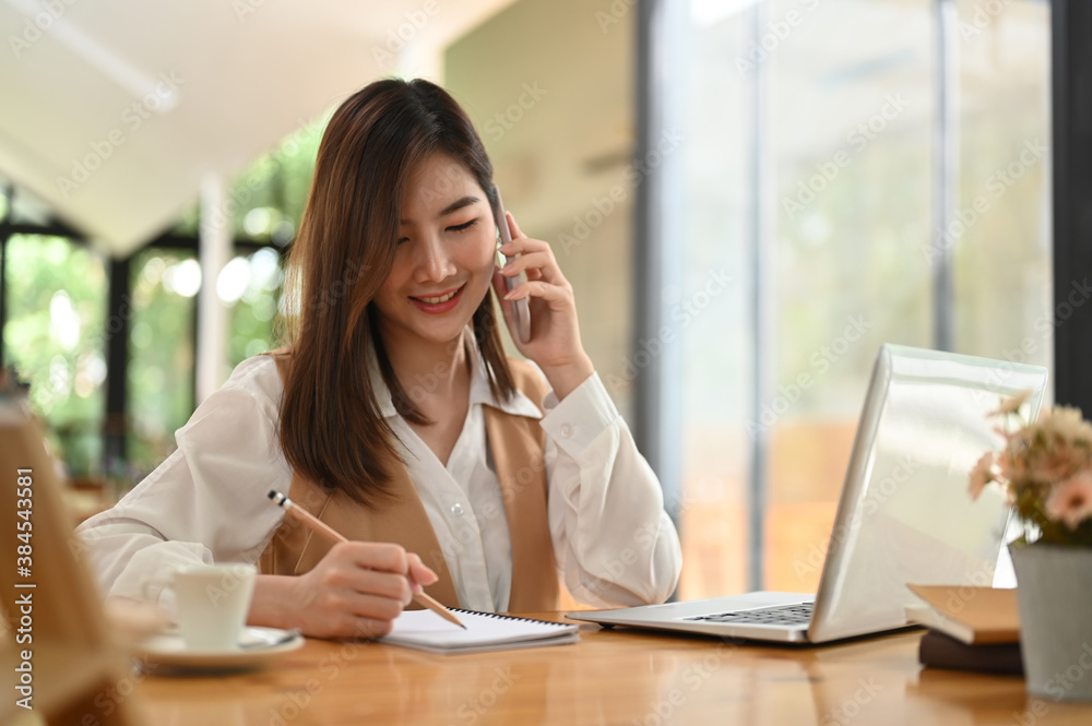Young female talking on the phone while writing on notebook at office. Young female talking on the phone while writing on notebook at office.