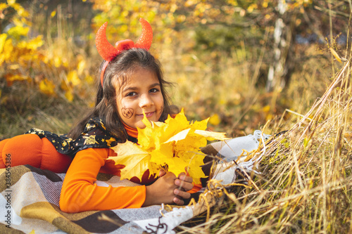 Halloween kids. Portrait of smilinggirl with brown hair in witch hat laying on autumn ground. photo