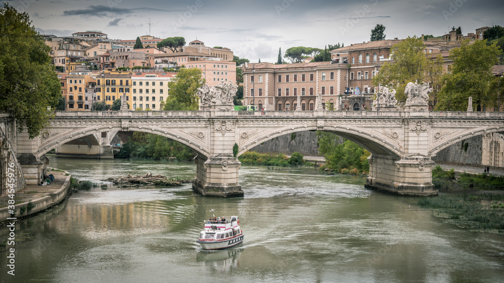 Panoramic view Emanuele II bridge over Tevere river in Rome, near Castel Sant'Angelo. Boat sails on the river of the Italian capital, historic buildings in the background. Tourism, art concept