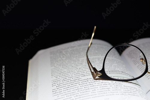 Reading glasses on open book and a dark background © equos