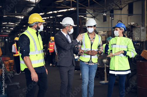 Leader or manager using tablet and meeting with engineer and technician while line walk in factory workplace, team wear face mask whine working at maintenance machine shop 