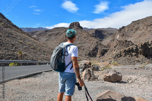 Young traveler photographed from the back, looking out over an arid mountain landscape.