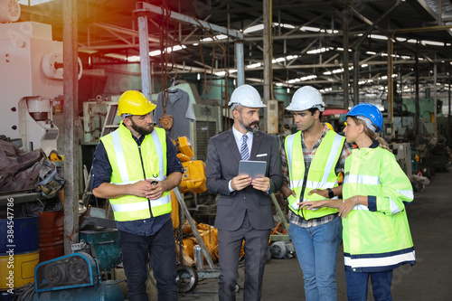 Leader or manager using tablet and meeting with engineer and technician while line walk in factory workplace, team wear face mask whine working at maintenance machine shop 
